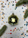 a shiny, metallic ornament with a reflective surface, surrounded by colorful confetti and pine branches.