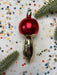A red ornament with a gold base is placed on a background of colorful confetti and green pine branches.
