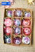 A cardboard box containing a set of twelve ornaments, each with a unique design and color. The ornaments are arranged in a grid pattern, with three rows and four columns. The background features handwritten text, which appears to be a list or description of the ornaments.