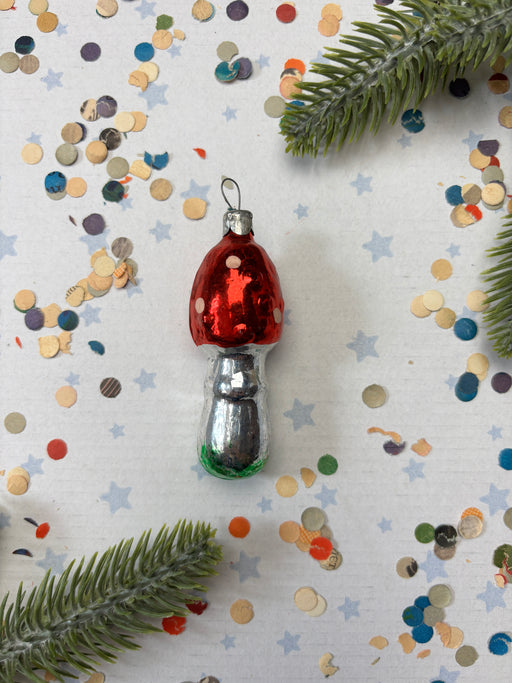 A red and silver ornament with white polka dots is placed on a white background, surrounded by scattered confetti and green pine branches.