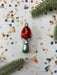 A red and silver ornament with white polka dots is placed on a white background, surrounded by scattered confetti and green pine branches.