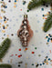 A pink Christmas ornament is placed on a white background with scattered confetti and green pine branches.