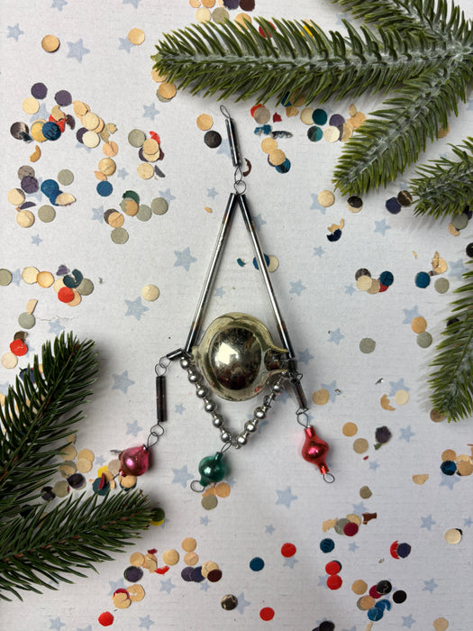 a Christmas ornament with a silver ball and a red ornament, surrounded by confetti and pine branches.