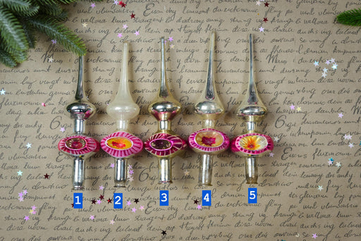 a collection of five ornamental objects, each with a unique design and color, arranged in a row on a textured surface. The objects are numbered 1 through 5, indicating their position in the row. The background of the image is filled with handwritten text, which appears to be a list or description of the objects.