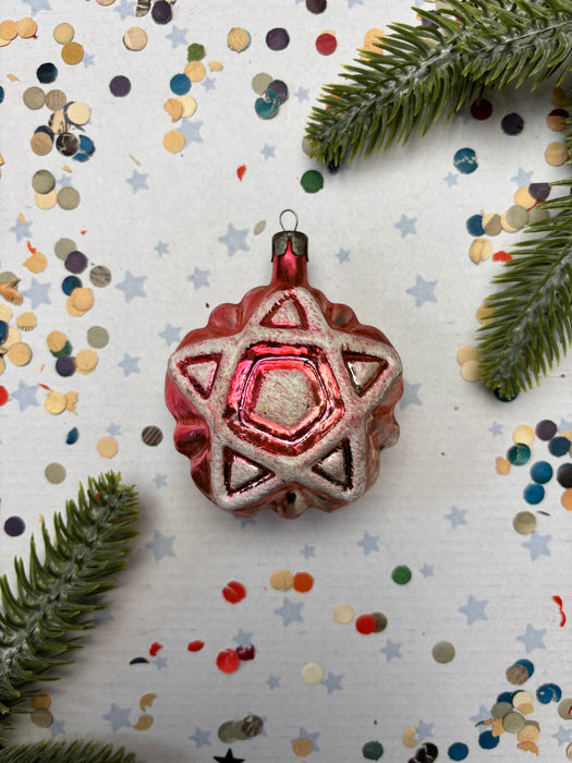 A red star-shaped ornament with a star at the center is surrounded by confetti and greenery, creating a festive and celebratory scene.