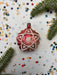 A red star-shaped ornament with a star at the center is surrounded by confetti and greenery, creating a festive and celebratory scene.