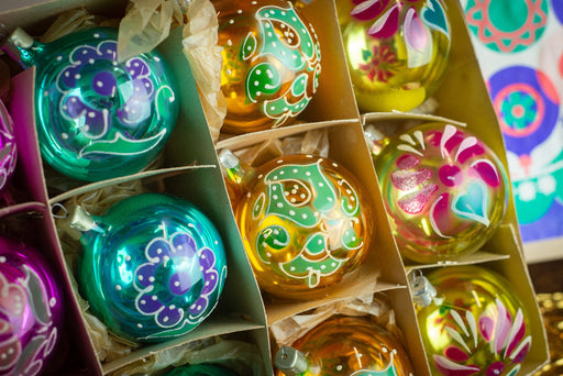 A close-up view of a collection of colorful Christmas ornaments, including glass baubles and baubles with intricate designs, arranged in a box.