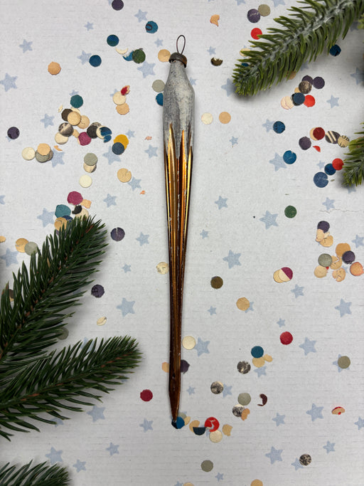 a metallic ornament with a long, curved shape, surrounded by colorful confetti and pine branches.