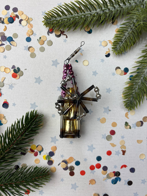 a decorative ornament with a metallic frame and a colorful, star-shaped design, surrounded by pine branches, confetti, and other festive elements.