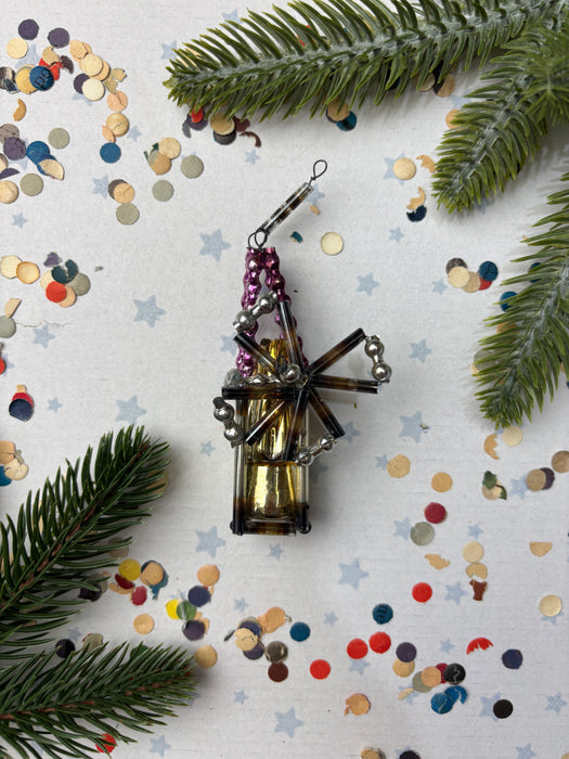 a decorative ornament with a metallic frame and a colorful, star-shaped design, surrounded by pine branches, confetti, and other festive elements.