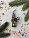 a decorative ornament with a metallic frame and a colorful, star-shaped design, surrounded by pine branches, confetti, and other festive elements.