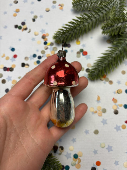 A hand is holding a red ornament with a polka dot design, surrounded by scattered confetti and a sprig of greenery.