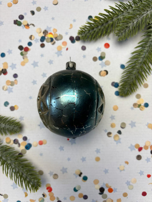 A shiny, black ornament with a cracked surface is surrounded by colorful confetti and a sprig of greenery, creating a festive and whimsical holiday scene.