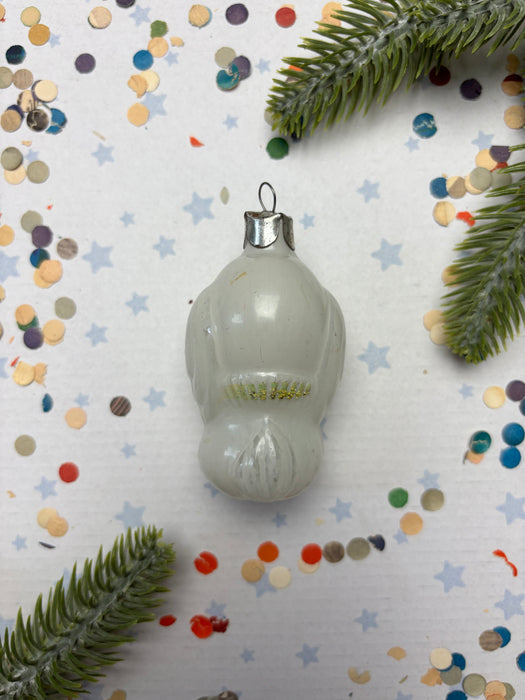 a white ornament with a silver hook, surrounded by colorful confetti and green pine branches.