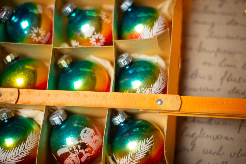 A close-up view of a box filled with colorful Christmas ornaments, with a ruler placed over the top of the box.
