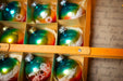 A close-up view of a box filled with colorful Christmas ornaments, with a ruler placed over the top of the box.