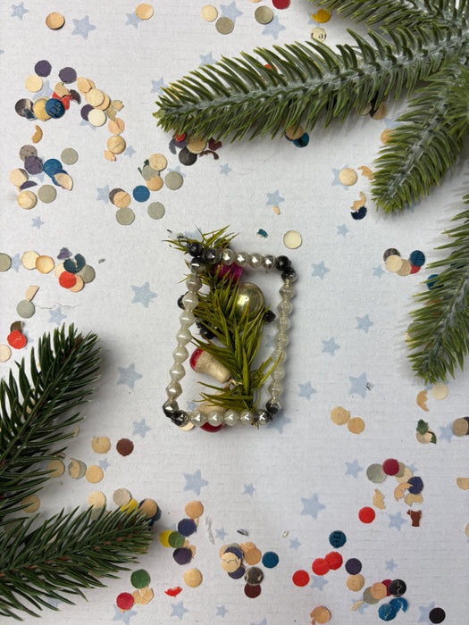 a festive arrangement of Christmas decorations, including pine branches, beads, and confetti, all set against a white background.