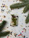 a festive arrangement of Christmas decorations, including pine branches, beads, and confetti, all set against a white background.