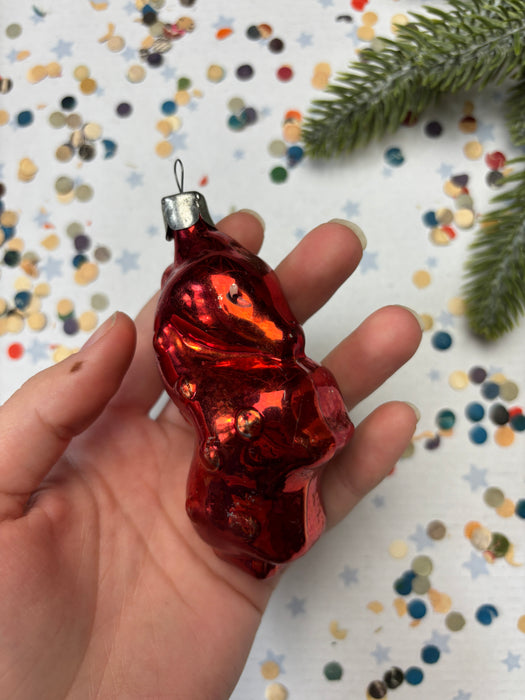 A hand holding a red ornament against a background of colorful confetti and a pine branch.