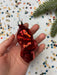 A hand holding a red ornament against a background of colorful confetti and a pine branch.