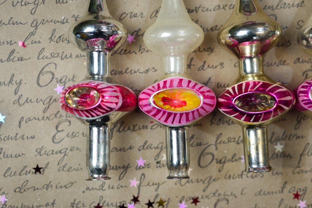 a close-up view of three decorative ornaments, each with a unique design and color, arranged on a surface with scattered stars. The ornaments appear to be made of glass or metal and are placed in a row, creating a visually appealing display.