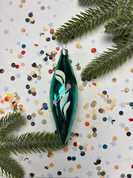 a green glass ornament with a white design, surrounded by colorful confetti and pine branches.