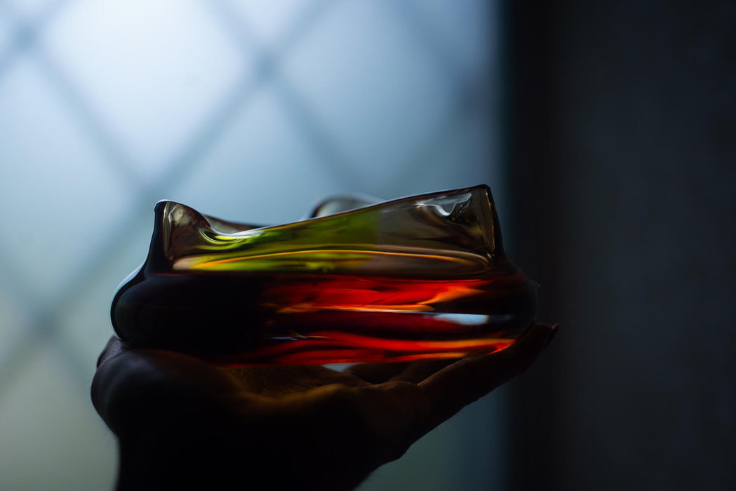 A hand holding a glass filled with a colorful liquid, possibly a cocktail or a drink, against a dark background.