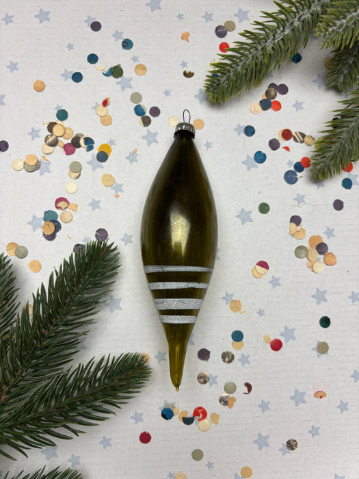 a green ornament with white stripes, surrounded by colorful confetti and pine branches.