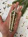 A hand holding a decorative ornament made of white and gold materials, with a metallic appearance. The background is a white surface with scattered confetti or small circular objects.