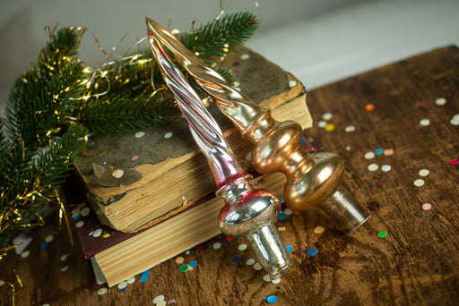 two ornate golden ornaments, one on top of a stack of books and the other on a wooden surface, surrounded by confetti.