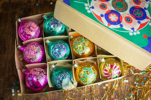 A box containing a dozen colorful Christmas ornaments, including pink, blue, green, and yellow balls, along with a decorative box lid.