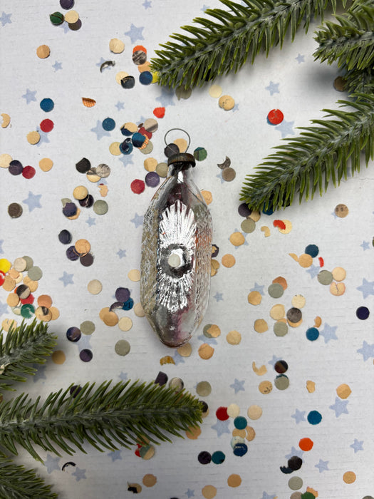 a vintage glass ornament with a star design, surrounded by colorful confetti and pine branches.