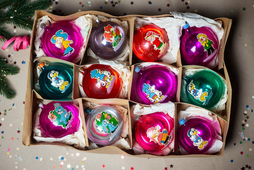 A box containing a dozen colorful Christmas ornaments, each with a unique design and character on it.