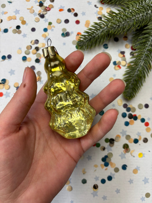 A hand holding a yellow glass ornament against a background of colorful confetti and a pine branch.