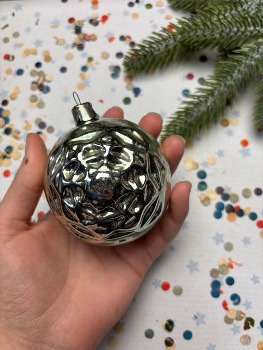 A hand holding a shiny silver ornament against a background of colorful confetti.