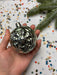 A hand holding a shiny silver ornament against a background of colorful confetti.
