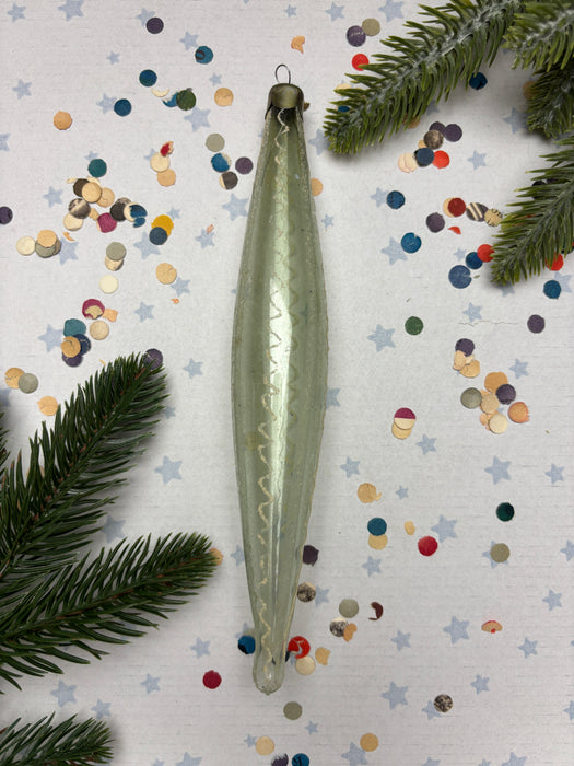 a green ornament with a curved shape, surrounded by colorful confetti and pine branches.