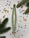 a green ornament with a curved shape, surrounded by colorful confetti and pine branches.