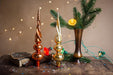 a festive Christmas scene with a vase of greenery, two ornate ornaments, and a book with confetti on a wooden surface.