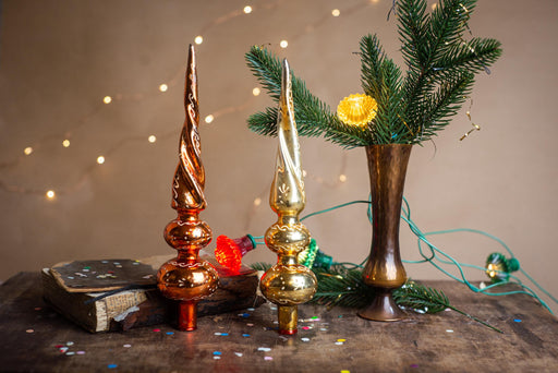 a festive Christmas scene with a vase of greenery, two ornate ornaments, and a book with confetti on a wooden surface.