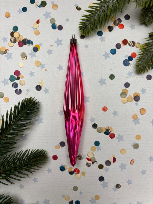 A pink glass ornament is surrounded by colorful confetti and pine branches on a white background.