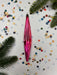 A pink glass ornament is surrounded by colorful confetti and pine branches on a white background.