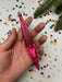 A hand holding a pink glass ornament against a background of colorful confetti and a pine tree branch.