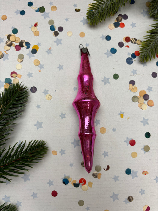 A pink ornament is placed on a white background, surrounded by colorful confetti and pine branches.