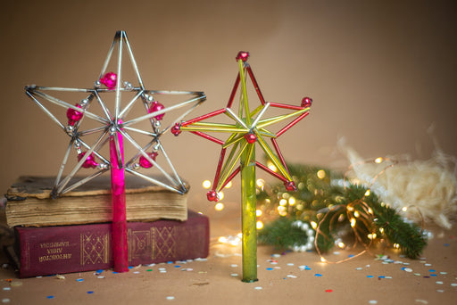 two star-shaped ornaments, one made of metal and the other of glass, placed on a table with books and confetti.