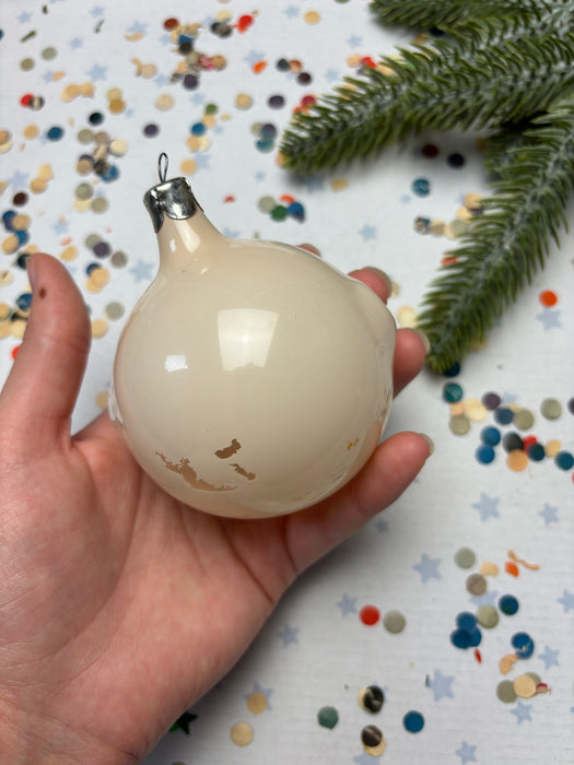 A hand holding a white ornament with a gold design, surrounded by colorful confetti on a festive background.