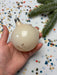 A hand holding a white ornament with a gold design, surrounded by colorful confetti on a festive background.