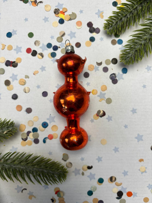 a red ornament with a shiny, reflective surface, surrounded by scattered confetti and pine branches.