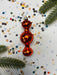 a red ornament with a shiny, reflective surface, surrounded by scattered confetti and pine branches.
