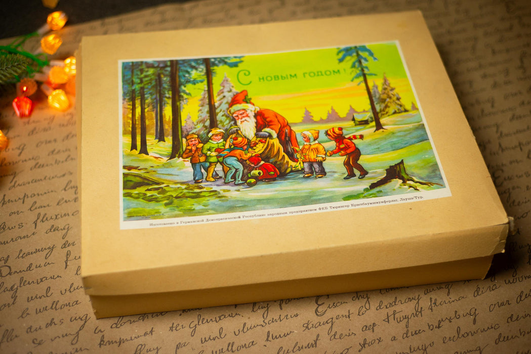 a Christmas-themed box with a painting of Santa Claus and children in a snowy forest.